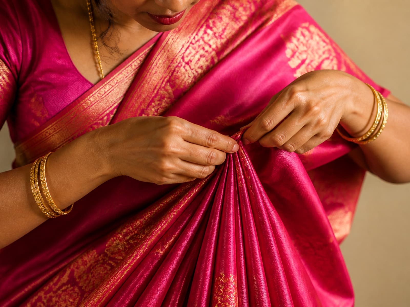 Hands carefully pleating a pink silk saree